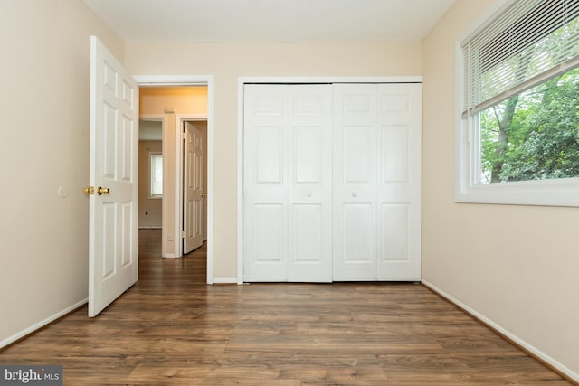 unfurnished bedroom with baseboards, dark wood-style flooring, and a closet