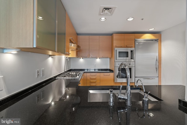 kitchen with stainless steel appliances, a sink, recessed lighting, dark stone countertops, and glass insert cabinets
