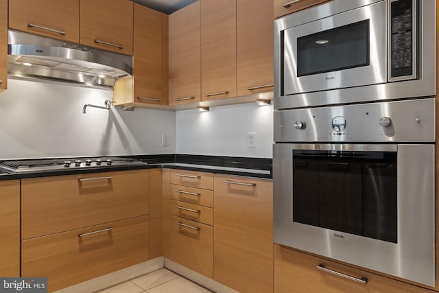 kitchen featuring stainless steel appliances, under cabinet range hood, light tile patterned floors, dark countertops, and modern cabinets