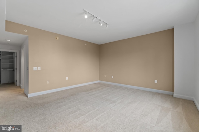 unfurnished room with light carpet, rail lighting, and baseboards