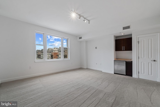 unfurnished living room featuring light carpet, rail lighting, and baseboards