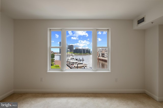 spare room with light colored carpet, baseboards, a water view, and a city view
