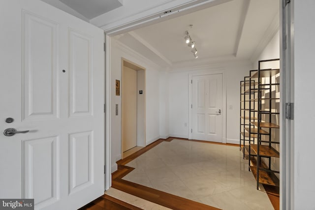 doorway with a raised ceiling, elevator, rail lighting, and baseboards