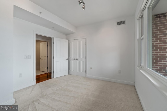 unfurnished bedroom featuring carpet, baseboards, a closet, and rail lighting