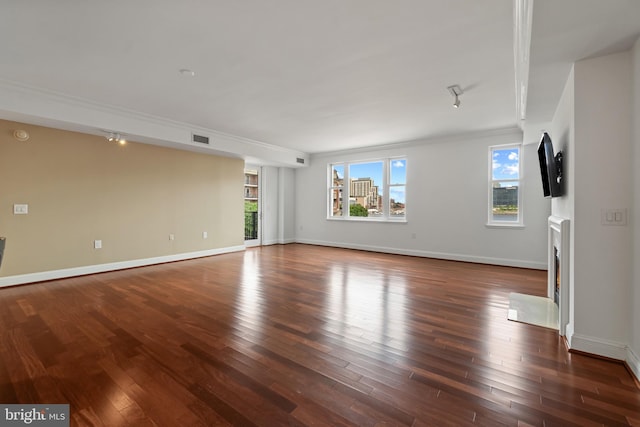 unfurnished living room with wood finished floors, baseboards, and ornamental molding