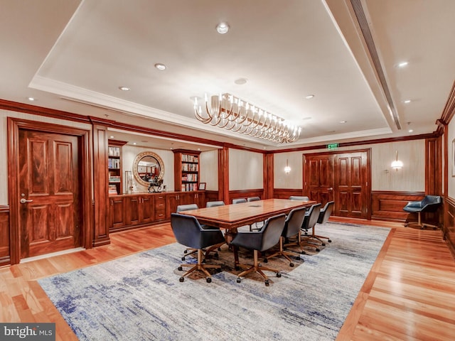 dining space featuring crown molding, light wood-style flooring, a chandelier, wood walls, and a wainscoted wall