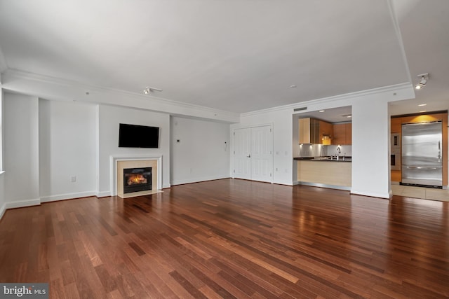 unfurnished living room with ornamental molding, wood finished floors, a fireplace with flush hearth, a sink, and baseboards