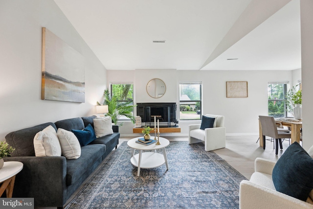 living room with lofted ceiling, baseboards, a glass covered fireplace, visible vents, and wood finished floors
