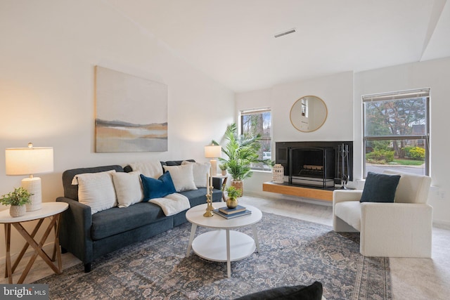 living area featuring lofted ceiling, a fireplace with raised hearth, visible vents, carpet floors, and baseboards