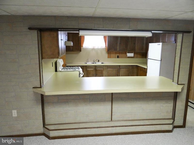 kitchen with a peninsula, a sink, white appliances, light colored carpet, and light countertops