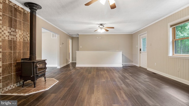 unfurnished living room featuring a wood stove, ceiling fan, dark wood-style floors, crown molding, and baseboards