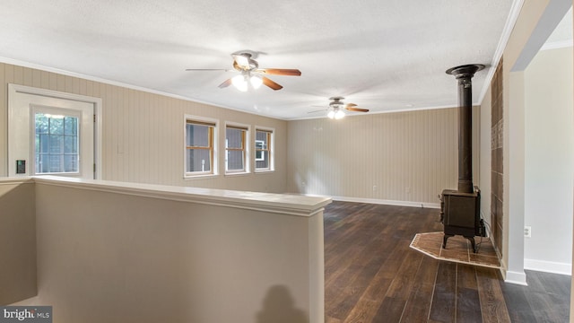 unfurnished living room featuring a wood stove, ornamental molding, dark wood-type flooring, a ceiling fan, and baseboards