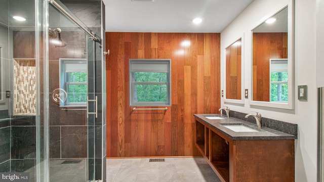 full bath featuring a shower stall, plenty of natural light, double vanity, and wood walls