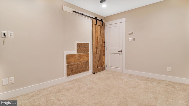 empty room with a barn door, carpet flooring, baseboards, and a ceiling fan
