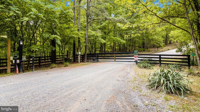view of road featuring a wooded view and a gate