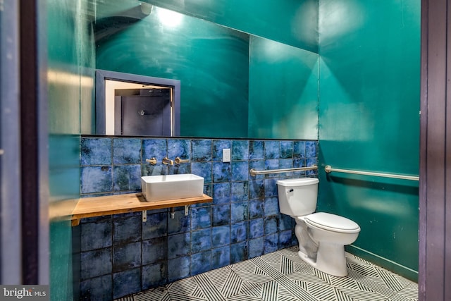 half bathroom with toilet, tile walls, tile patterned flooring, and a wainscoted wall