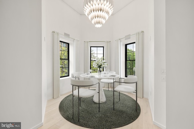 dining space with a chandelier, light wood-type flooring, baseboards, and a towering ceiling