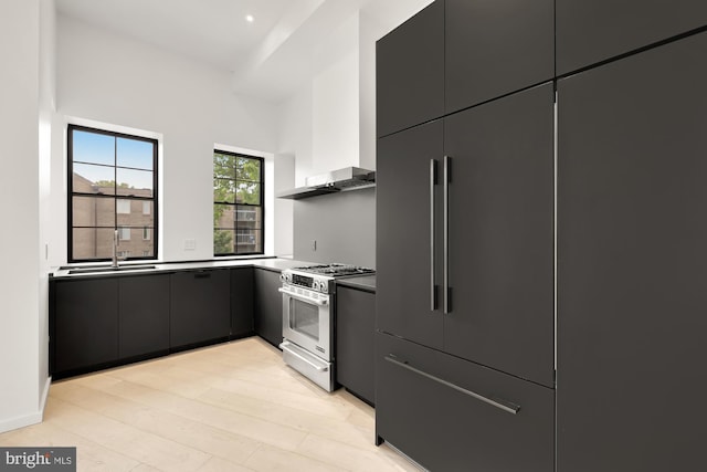 kitchen featuring stainless steel range with gas stovetop, dark countertops, a sink, modern cabinets, and light wood-style flooring