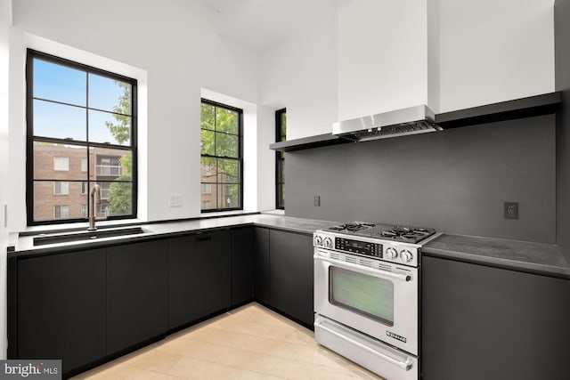 kitchen with stainless steel gas range, a sink, dark cabinetry, wall chimney range hood, and dark countertops