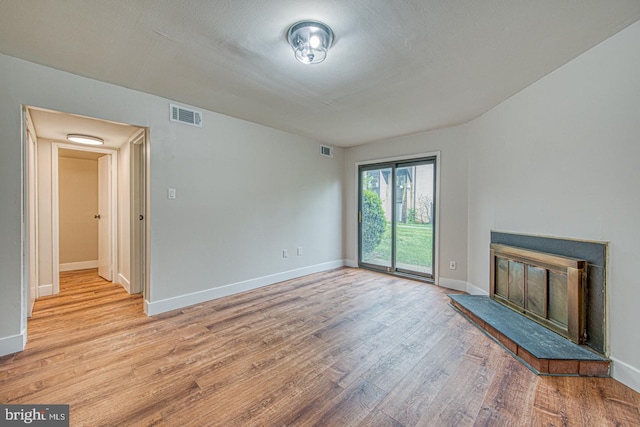 unfurnished living room featuring light wood finished floors, a glass covered fireplace, baseboards, and visible vents
