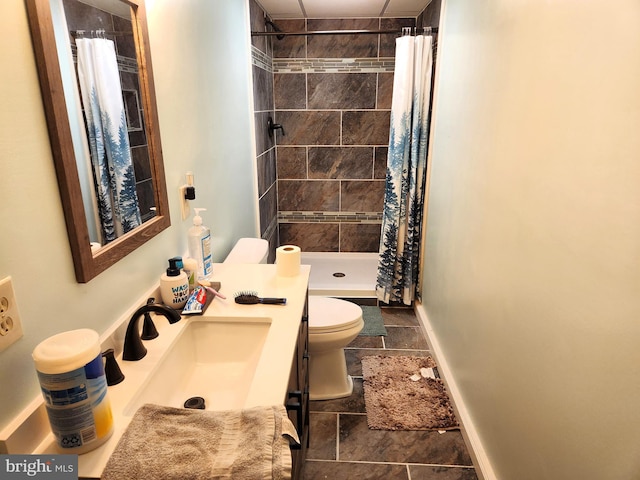 full bath with toilet, stone tile flooring, vanity, baseboards, and tiled shower