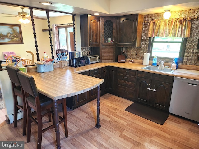 kitchen featuring light wood-style flooring, a sink, stainless steel dishwasher, light countertops, and tasteful backsplash