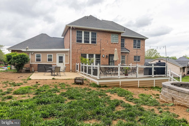 back of property featuring brick siding, a deck, a patio, and a shingled roof
