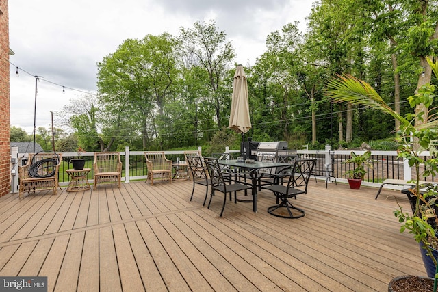 wooden deck with outdoor dining area, grilling area, and view of wooded area