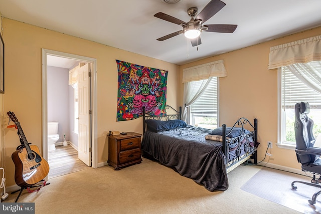 carpeted bedroom with ensuite bath, baseboards, and ceiling fan