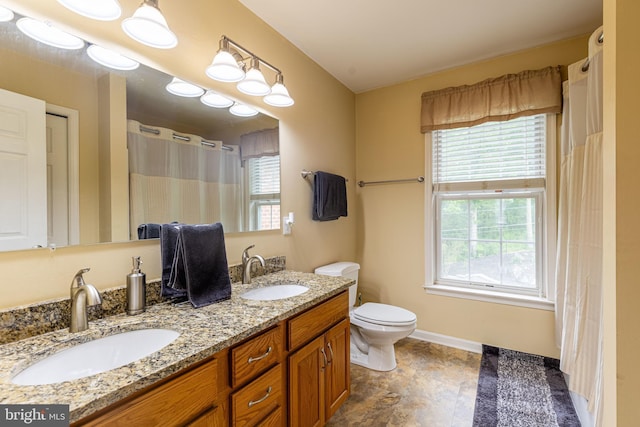bathroom featuring toilet, double vanity, and baseboards
