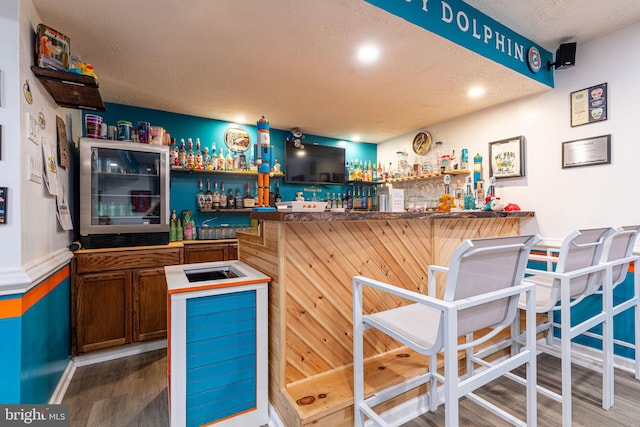 indoor wet bar with wood finished floors, beverage cooler, a textured ceiling, and baseboards