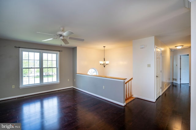 spare room featuring dark wood-style flooring, ceiling fan with notable chandelier, and baseboards