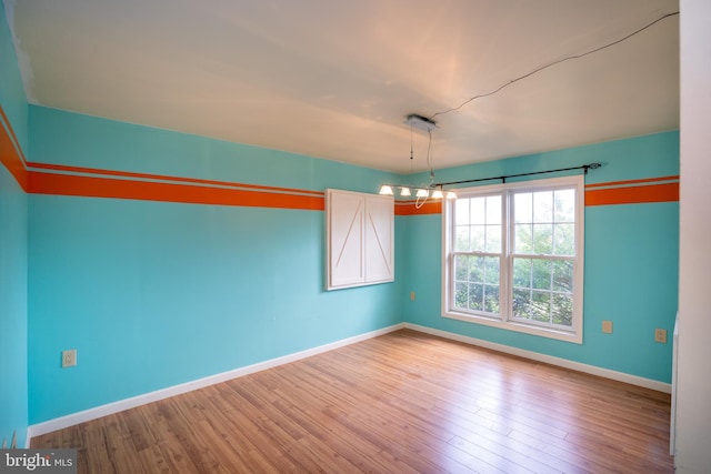 unfurnished dining area featuring baseboards, a chandelier, and wood finished floors