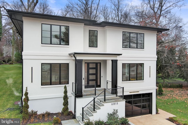modern farmhouse style home with stucco siding, an attached garage, a front lawn, and concrete driveway