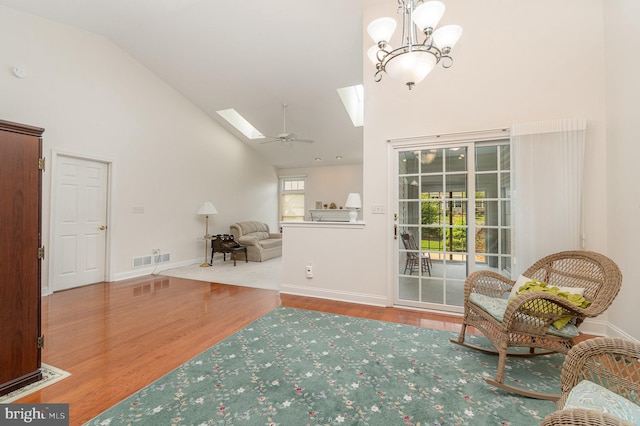 living area featuring high vaulted ceiling, a skylight, wood finished floors, a chandelier, and baseboards