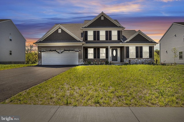 view of front facade featuring stone siding, a garage, a shingled roof, a front yard, and driveway