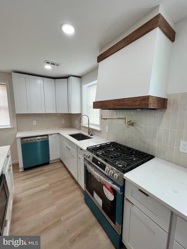 kitchen with a sink, visible vents, dishwasher, stainless steel gas range, and custom range hood