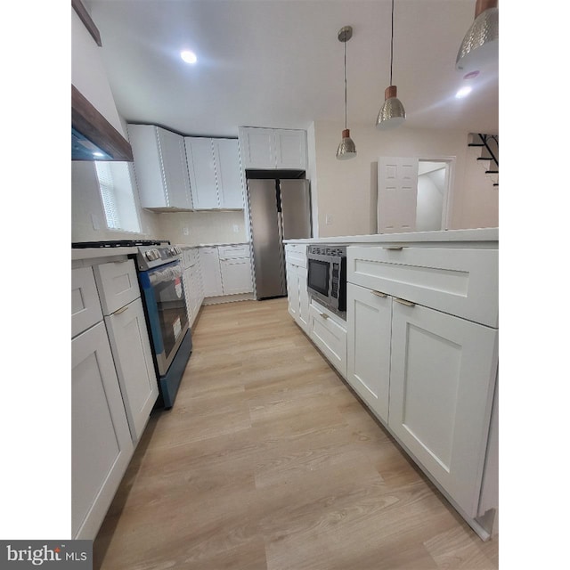 kitchen featuring light countertops, appliances with stainless steel finishes, pendant lighting, and light wood-type flooring