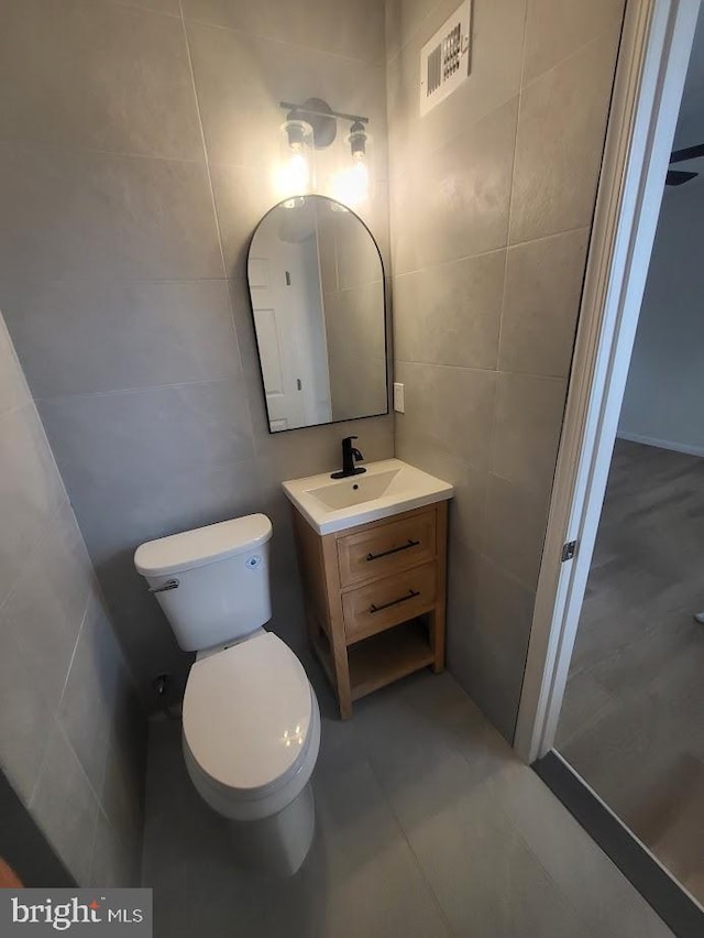 half bath featuring tile walls, toilet, visible vents, and vanity