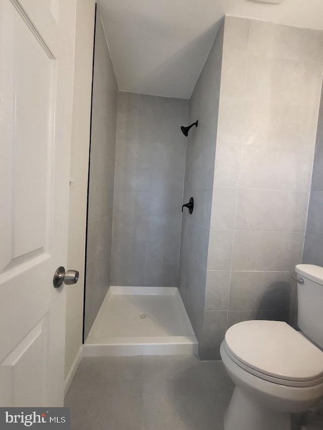 bathroom with a stall shower, tile walls, and toilet