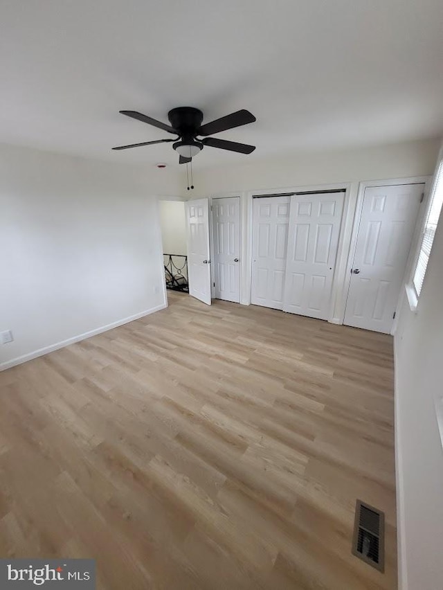 unfurnished bedroom with light wood finished floors, multiple closets, visible vents, baseboards, and ceiling fan