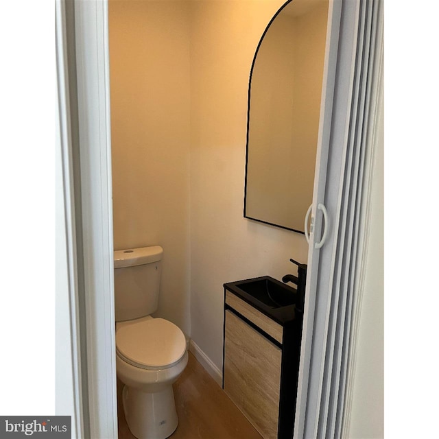 bathroom with toilet, baseboards, wood finished floors, and a sink