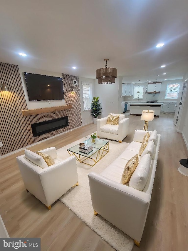 living room with a notable chandelier, recessed lighting, wood finished floors, and a glass covered fireplace