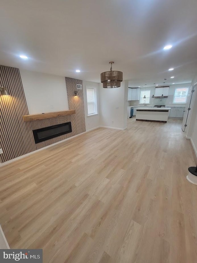 unfurnished living room with light wood finished floors, baseboards, a glass covered fireplace, and recessed lighting
