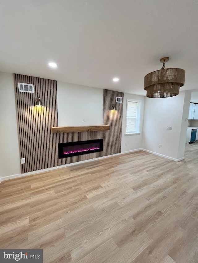 unfurnished living room featuring recessed lighting, baseboards, a glass covered fireplace, and wood finished floors