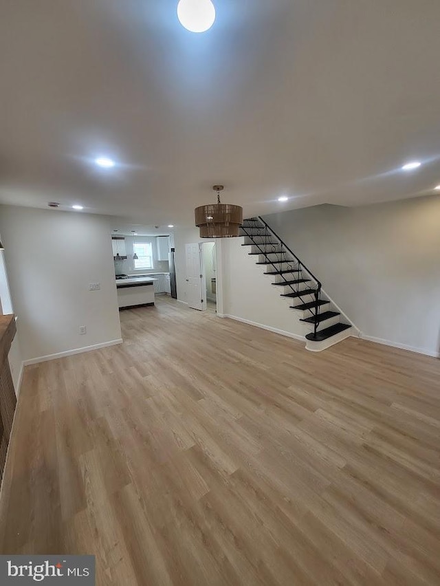 unfurnished living room with a notable chandelier, stairway, baseboards, light wood-style floors, and recessed lighting