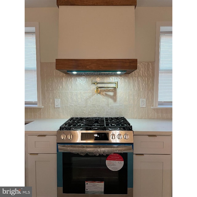 kitchen with stainless steel range with gas cooktop, backsplash, light countertops, and premium range hood