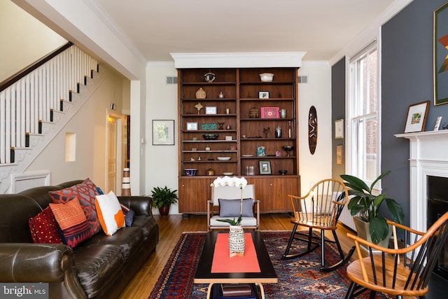 living area with crown molding, visible vents, dark wood-style flooring, and stairs