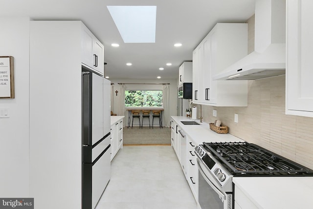 kitchen featuring appliances with stainless steel finishes, a sink, wall chimney range hood, tasteful backsplash, and white cabinets