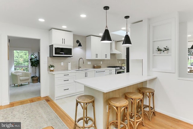 kitchen featuring white appliances, light wood-style flooring, a breakfast bar, a sink, and white cabinetry